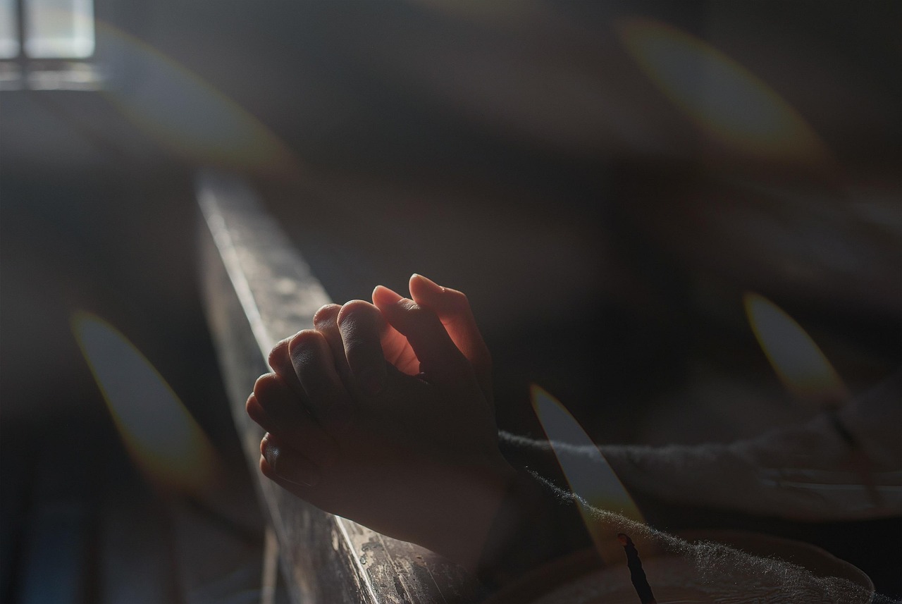 Mãos em oração com vela acesa, símbolo de fé e devoção a São Josemaria Escrivá